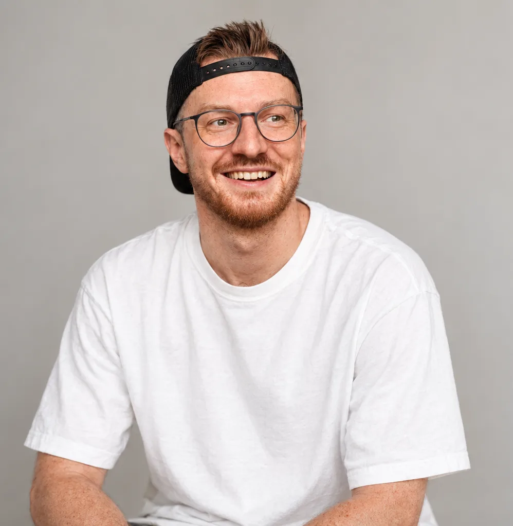 Markus Kober lacht, im weißen T-Shirt mit Cap vor grauem Hintergrund
